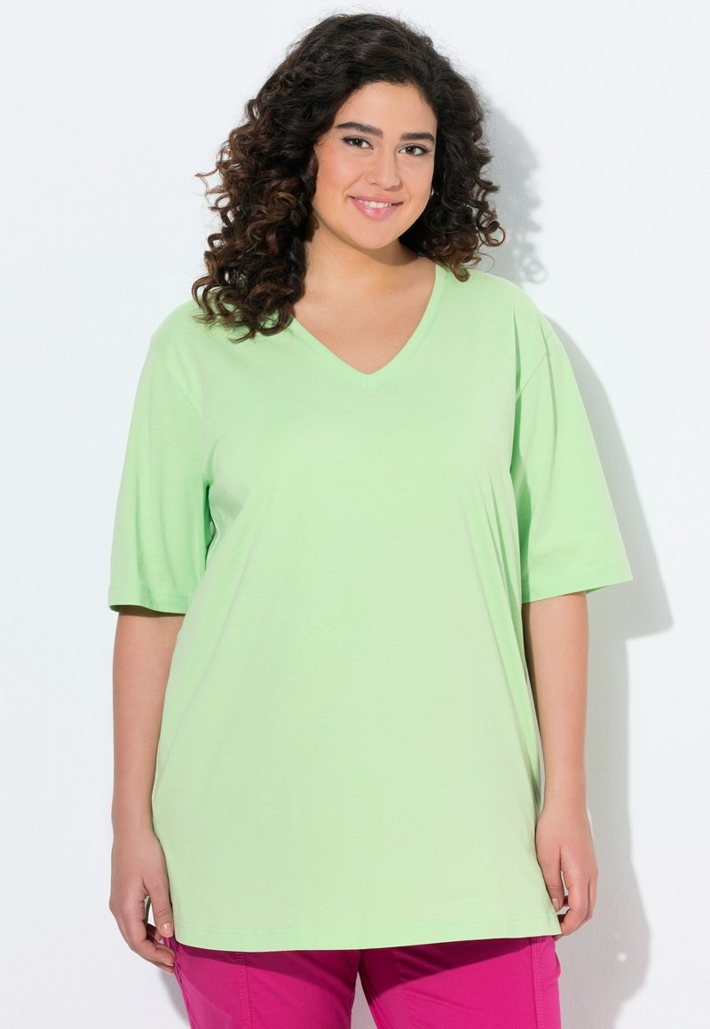 T-shirt a V scollo, maniche corte in cotone verde chiaro con una vestibilità rilassata, abbinato a pantaloni rosa, su sfondo bianco.