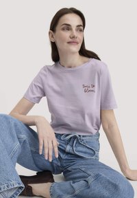 Lila katoenen T-shirt met korte mouwen, ronde hals en "tijd om te bloeien" geborduurd in het rood. Draag het met lichtblauwe spijkerbroek.