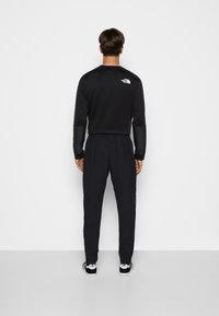 Svart långärmad topp och matchande träningsoverallbyxor. Tyget ser slätt ut; toppen har en logotyp på ryggen. Byxorna har en elastisk midja.