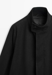 Cappotto in lana nera con collo alto, chiusura doppio bottone e design minimalista con una texture liscia.