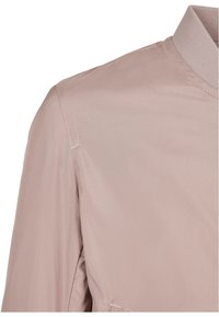 Light mauve jacket with a ribbed collar and visible stitched seams on the shoulder and upper arm areas.