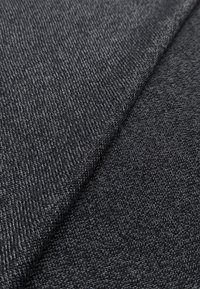 Dunkelgrauer Stoff mit feiner, strukturierter Webart. Das Material weist subtile Farbvariationen auf, die eine Tiefe an der Oberfläche erzeugen.