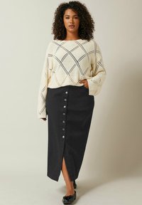 Maglione lavorato a maglia crema con motivo a rombi, abbinato a una gonna midi nera con bottoni e spacco frontale, completato da ballerine nere.
