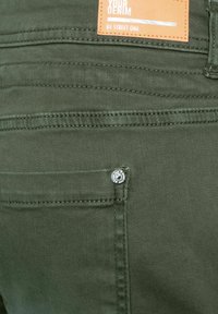 Pantalones de mezclilla verde oliva con un acabado texturizado, que presentan un pequeño bolsillo y herrajes plateados. La etiqueta de la marca muestra "YOUR DENIM by STREET ONE."