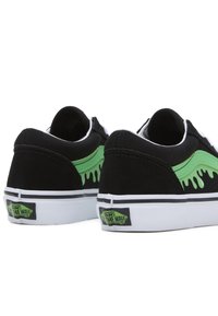 Mustat mokkanahka sneakersit, joissa on vihreät liekkigrafiikat sivuilla, valkoiset kumipohjat ja Vans-logo-tunnus kantapäässä.