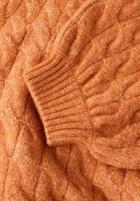 Strikket sweater i en varm orange farve, med et kabelmønster og ribbede manchetter, lavet af et blødt, tekstureret materiale.