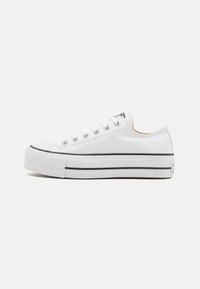 Weiße Leinensneaker mit niedrigem Schnitt, runder Spitze, schwarzer Gummisohle, Metallösen und kontrastierendem schwarzen Streifen um die Sohle.