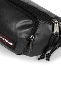 Černá nylonová ledvinka s texturovaným povrchem, vybavená dvojitými zipovými přihrádkami, nastavitelnými kordy a logem na přední straně.