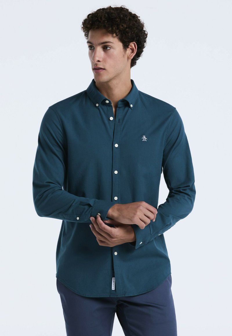 Teal langwerpig overhemd met knoopjes en een puntige kraag, witte knopen en een klein logo geborduurd op de borst. Gladde textuur, op maat gemaakte pasvorm.