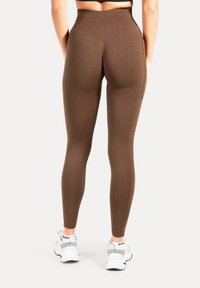 Leggings marroni a vita alta con motivo a coste testurizzato e tasche laterali, abbinati a scarpe sportive bianche.