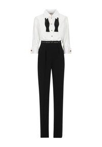 Camicia bianca a maniche lunghe con papillon nero, bottoni dorati; pantaloni neri a vita alta con pieghe e una cintura nera con dettagli di branding.