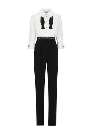 Camicia bianca a maniche lunghe con papillon nero, bottoni dorati; pantaloni neri a vita alta con pieghe e una cintura nera con dettagli di branding.