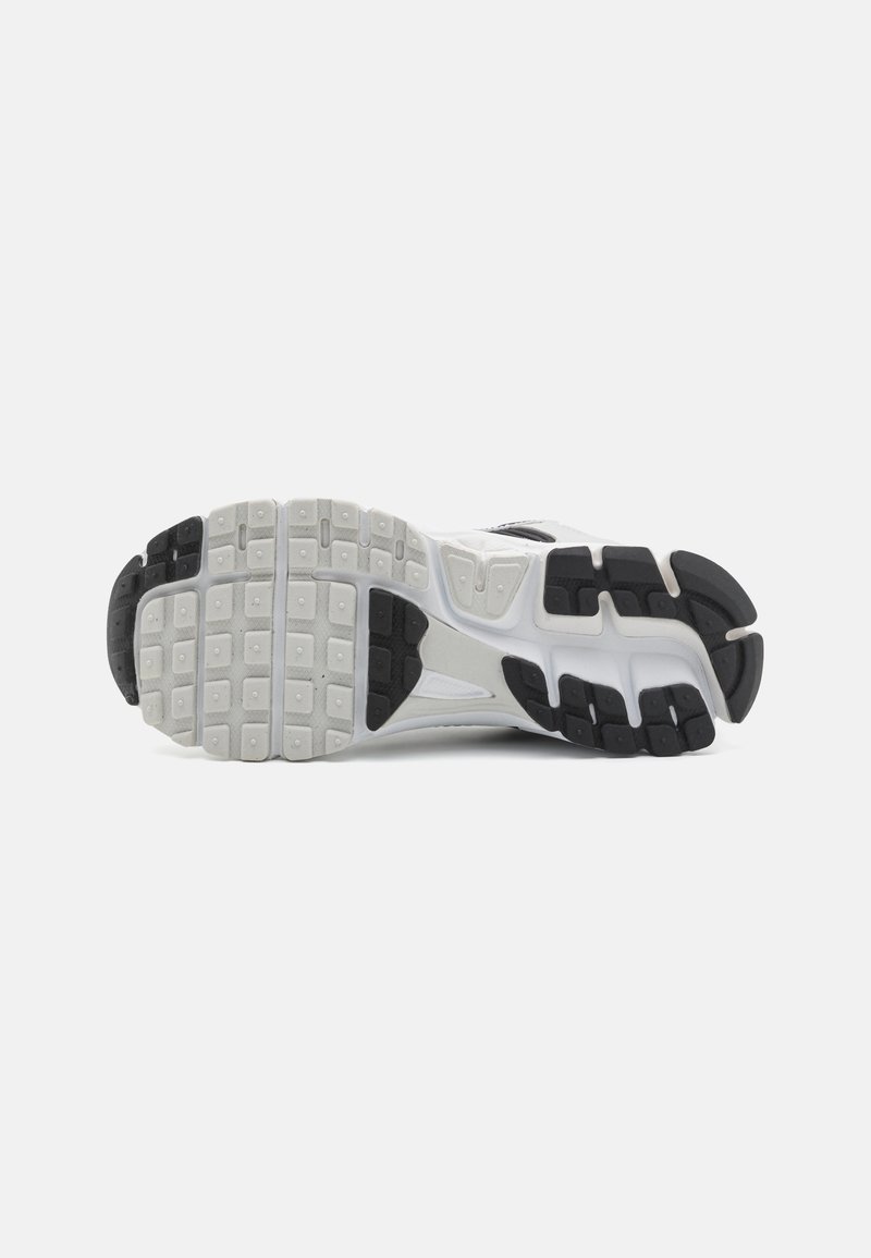 Semelle de chaussure de sport, avec un mélange de caoutchouc blanc et noir, présentant des motifs de grip texturés, des zones renforcées et un design contourné.