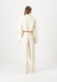 Cropped cream jacket with long sleeves and an embossed pattern, paired with matching high-waisted pants, featuring a smooth texture and simple design.