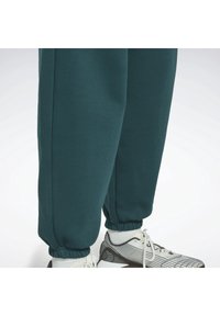 Tealgröna mjukisbyxor med elastiska muddar och en slät textur. Bärs med en lätt sneakers med svartvitrandigt mönster.