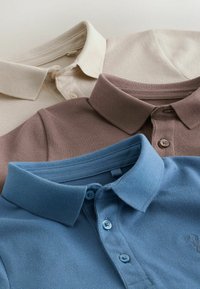 Tre poloer i lys beige, brun og blå. Hver har et tekstureret stof, krave, to knapper og et logo på den blå skjorte.