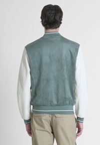Giacca bomber in suede verde con maniche in pelle bianca, polsini e orlo a coste. Presenta una leggera lucentezza e dettagli a righe sul colletto.