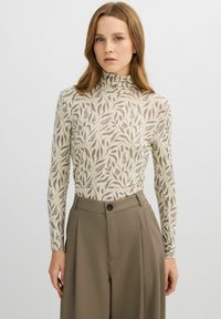 Top de manga larga con cuello alto, con fondo beige y patrones marrones de hojas botánicas. Tejido suave con silueta ajustada.