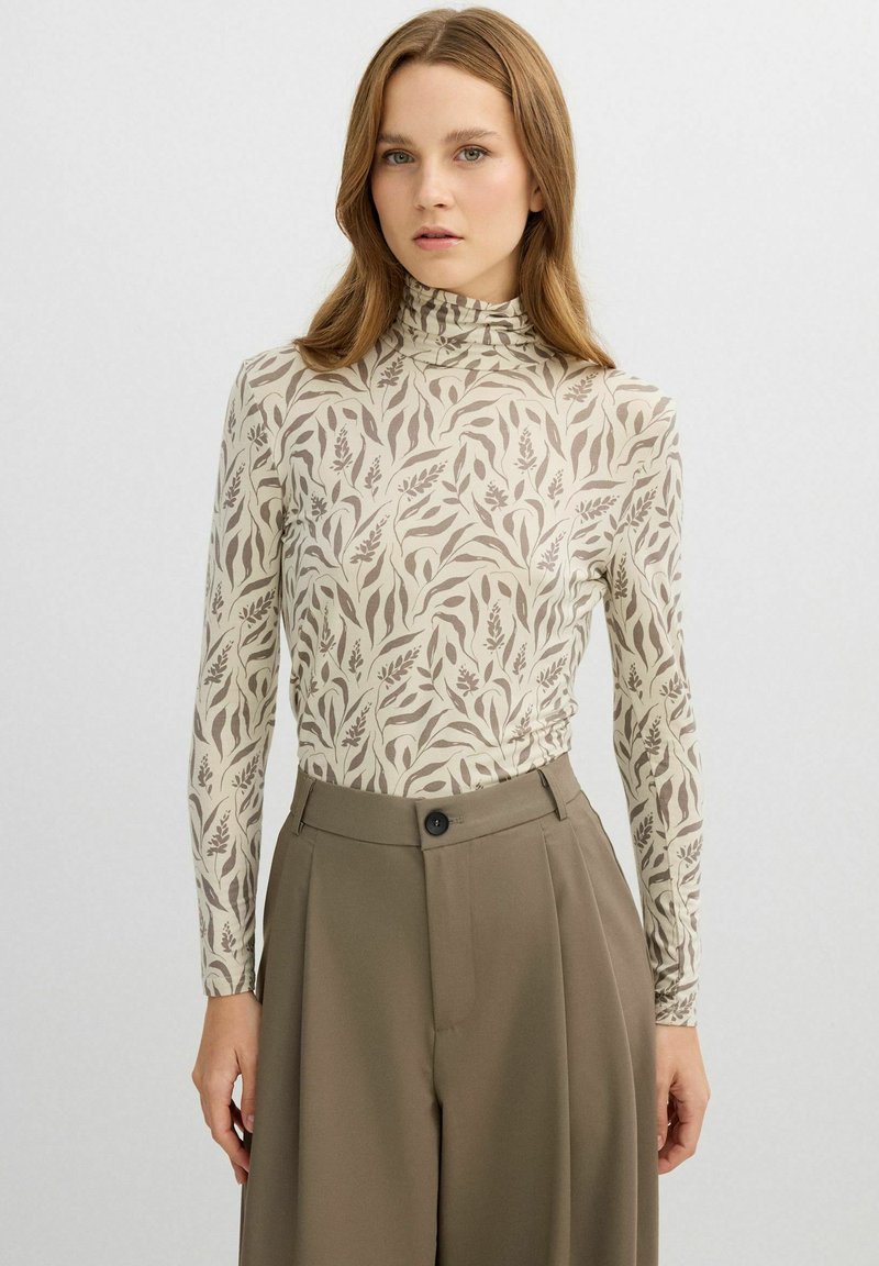 Top de manga larga con cuello alto, con fondo beige y patrones marrones de hojas botánicas. Tejido suave con silueta ajustada.