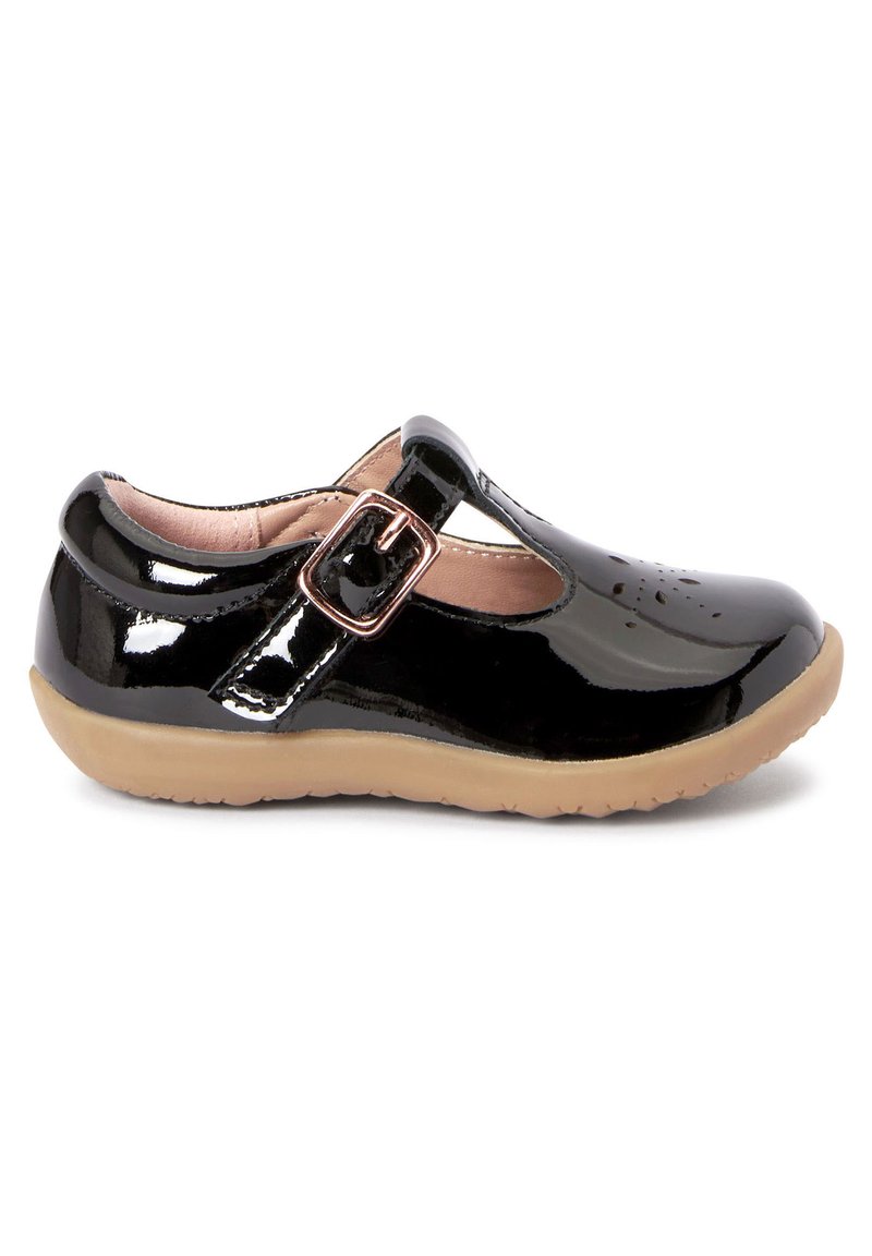 Schwarze Lackleder-Mary-Jane-Schuhe mit einer tanfarbenen Gummisohle, verstellbarem Riemen mit Schnalle und ausgeschnittenem Blumenmuster an der Zehenpartie.