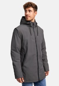 Veste à capuche grise avec fermeture éclair à l'avant et poches latérales. Elle présente une texture lisse et une coupe légèrement plus longue. Design décontracté.