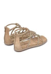 Sandalias de ante beige con correas cruzadas, adornadas con pequeños acentos metálicos y una suela plana y brillante. Detalle de cremallera en la parte trasera.