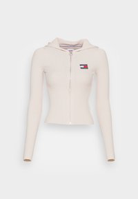 Ribbed, zip-up hoodie in light beige. Features long sleeves, fitted design, and a small "Tommy Jeans" logo patch on the left chest.