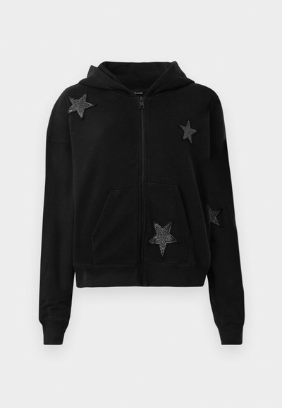 Sudadera negra con cremallera, con bolsillos frontales y capucha, decorada con cuatro parches de estrellas negras adornados con pequeñas cuentas.