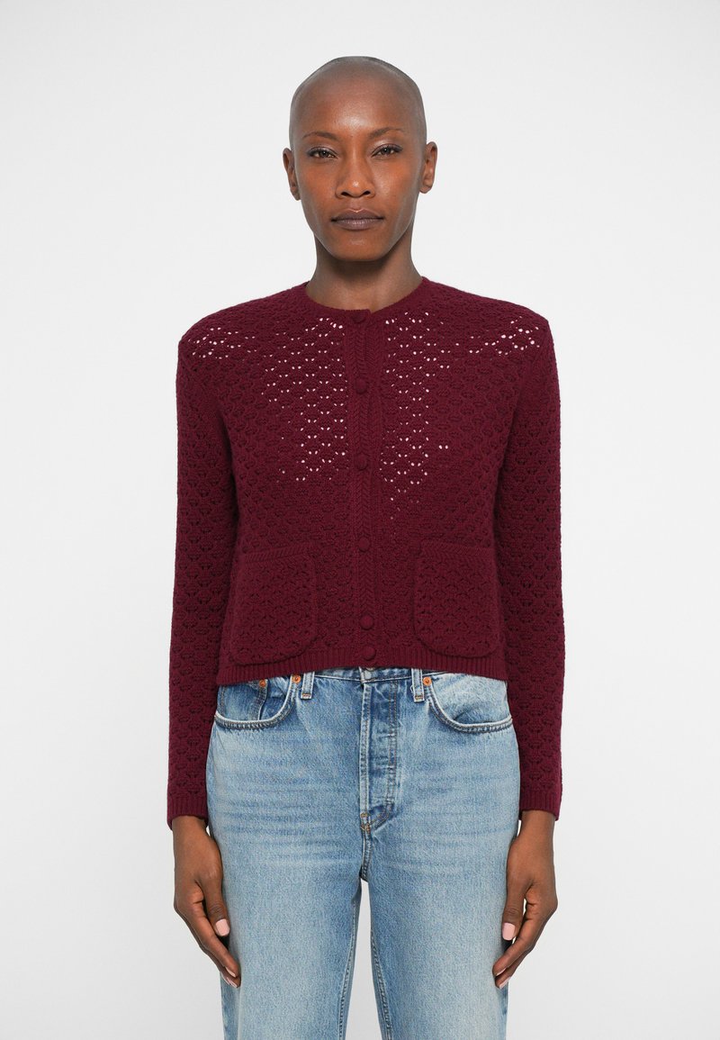 Cardigã tricotado em bordô com um padrão texturizado, gola redonda, seis botões e dois bolsos frontais, combinado com jeans azul claro.