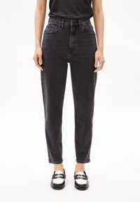 High-waisted black jeans in a slim fit, featuring front pockets, subtle texture, and stitched detailing, paired with black and white loafers.