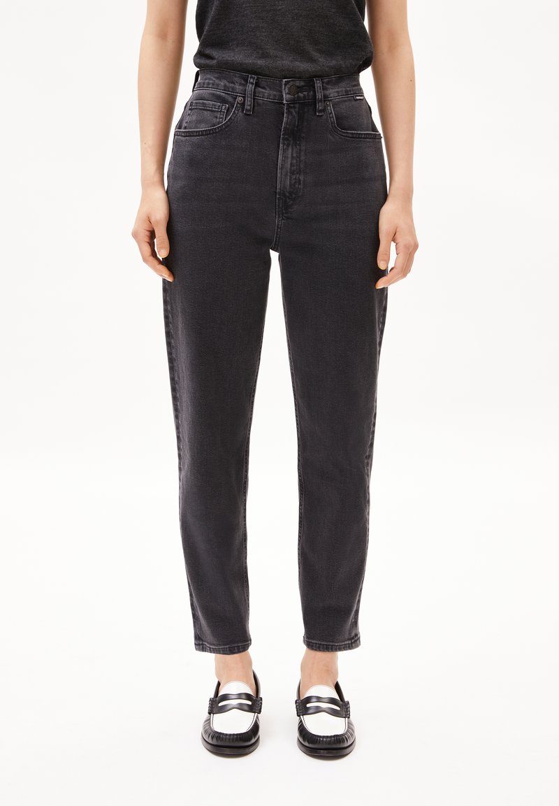 High-waisted black jeans in a slim fit, featuring front pockets, subtle texture, and stitched detailing, paired with black and white loafers.