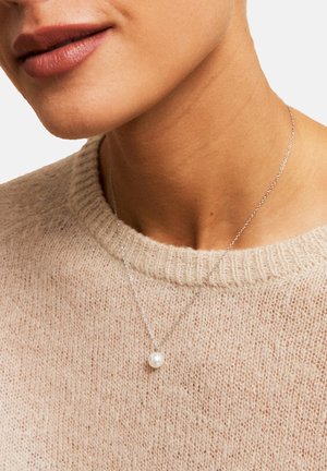 Collana d'argento con un unico pendente di perla bianca rotonda, indossata sopra un pullover in maglia beige chiaro. In primo piano il collo e lo scollo.