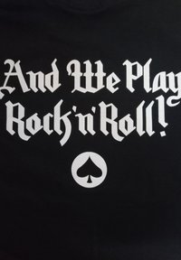 Camiseta negra con un gran texto gótico en blanco que dice "¡Y tocamos rock and roll!" debajo de un símbolo de trébol blanco.