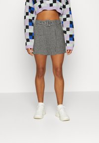 Mini gonna a scacchi bianco e nero con dettaglio della cintura, caratterizzata da un tessuto testurizzato. Abbinata a un maglione cropped multicolore e sneakers bianche.