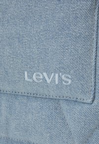 Ljusblå denimtyg med en sydd Levi's-logga i vitt. Texturen är slät med synliga vävmönster och sömmar.