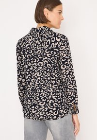 Blus med långa ärmar som har en marinblå botten med beige leopardfläckar, framfållar och knappslutningar vid ärmarna. Slät tygkvalitet med en avslappnad passform.