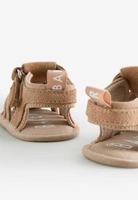 Tan ruskindssandaler med et åbent design, udstyret med en polstret sål, Velcro remme og en syet kant. Logo mærke på hælen.