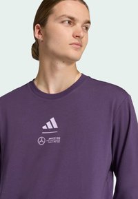 Purple sweatshirt with a crew neckline. Features white Adidas and AMG Petronas logos on the chest. Smooth fabric texture and casual fit.