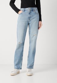 Lys blå denim jeans med rett passform, høy midje, to lommer og slitte detaljer ved knærne. Kombinert med hvite joggesko.