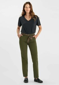 Donkergrijze V-hals t-shirt, olijfgroene broek met een luipaardprint riem en zwarte schoenen. De stof lijkt glad met een getailleerde fit.