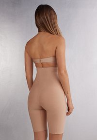 Beige bodysuit met een strapless ontwerp, voorzien van een uitgesneden achterkant en een lengte tot halverwege de dij. Gladde textuur met een getailleerde silhouette.