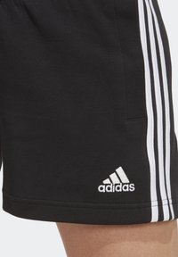 Svarta sportshorts med vita sidosträck och en broderad Adidas-logga. Tillverkade av ett mjukt, stretchigt material för komfort.