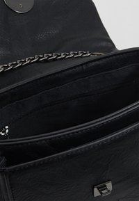 Černá kožená kabelka s texturovaným povrchem, stříbrným řetízkovým popruhem a vnitřní kapsou na zip. Obsahuje kovové zacvakávací uzavírání a vnitřní podšívku.