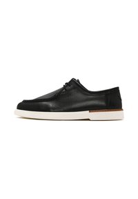 Chaussure en cuir noir au toucher lisse, à bout arrondi, semelle en caoutchouc blanche et accent marron près du talon. Elle dispose de lacets pour un maintien sécurisé.
