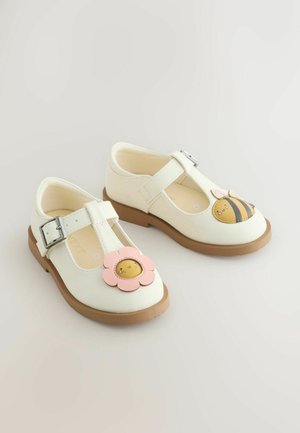 Fehér bőrcipő barna talppal, minden lábujjnál rózsaszín virággal és sárga méh mintával. Csattos pánt a biztos rögzítésért.