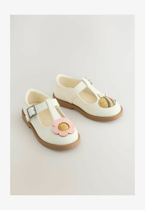 White leather shoes with a brown sole, featuring a pink flower and a yellow bee design on each toe. Buckle strap for secure fit.