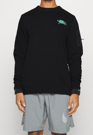 Person wearing black long-sleeve shirt with small teal text on chest and gray shorts with a white swoosh logo on left leg.