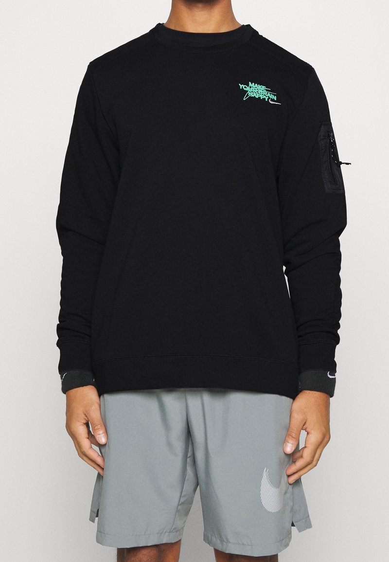 Personne portant une chemise noire à manches longues avec un petit texte bleu sarcelle sur la poitrine et un short gris avec un logo swoosh blanc sur la jambe gauche.