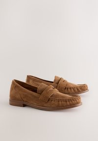 Paire de mocassins pour hommes en daim marron avec talons bas et détails cousus sur un fond clair uni.