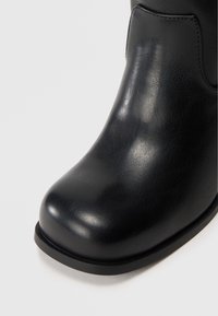 Čierne členkové topánky s hladkým vzhľadom z faux kože, zaoblenou špičkou a nízkou plochou podrážkou. Minimálne šitie a elegantný dizajn.